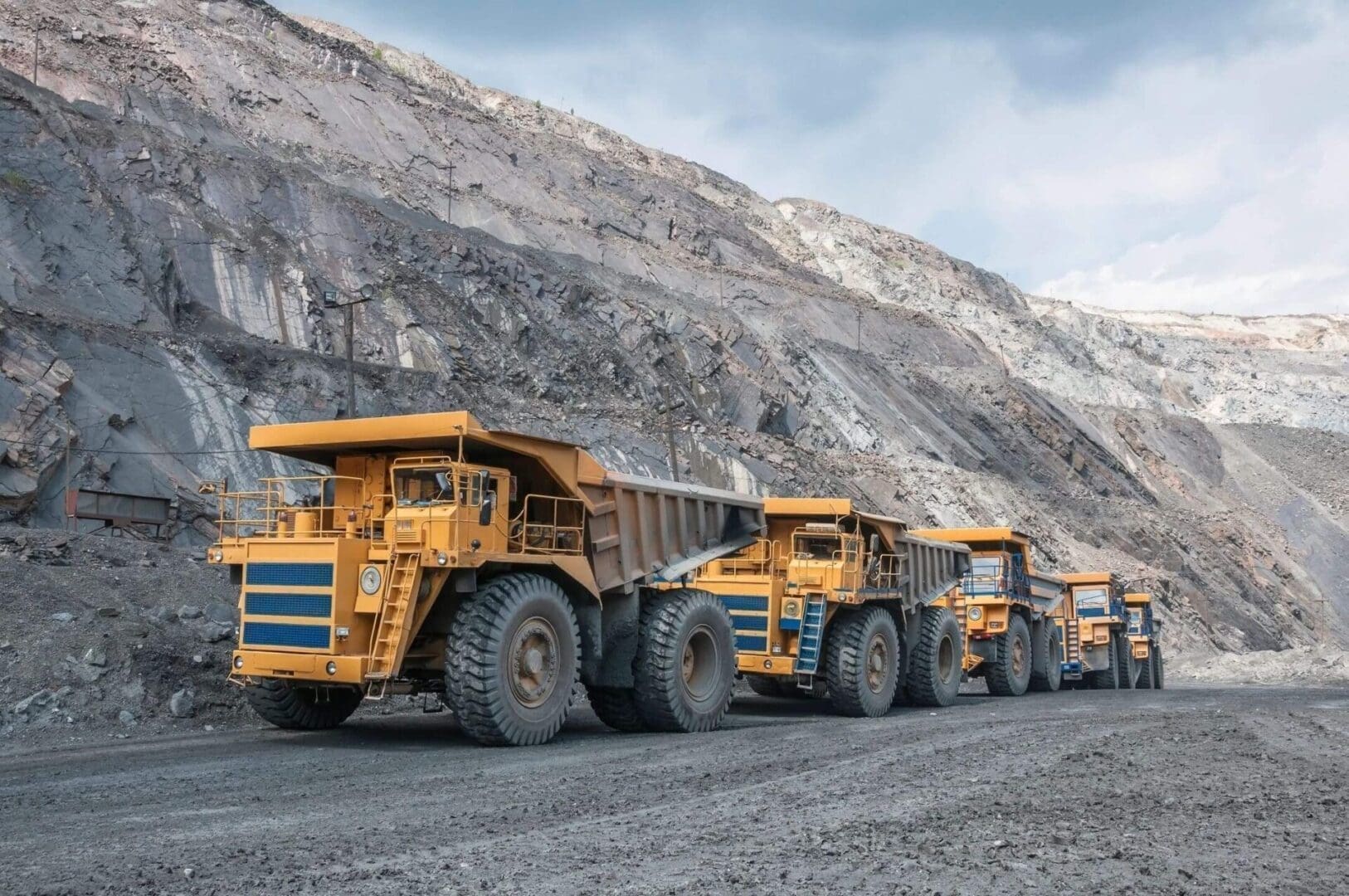 A group of large trucks parked on top of a gravel road.