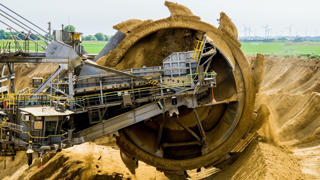 A large machine is in the dirt near some grass.